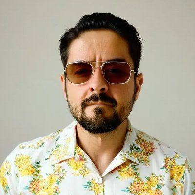 Arturo Tafoya, el autor: cabello oscuro, barba, lentes de aviador polarizados, camisa blanca con flores amarillas